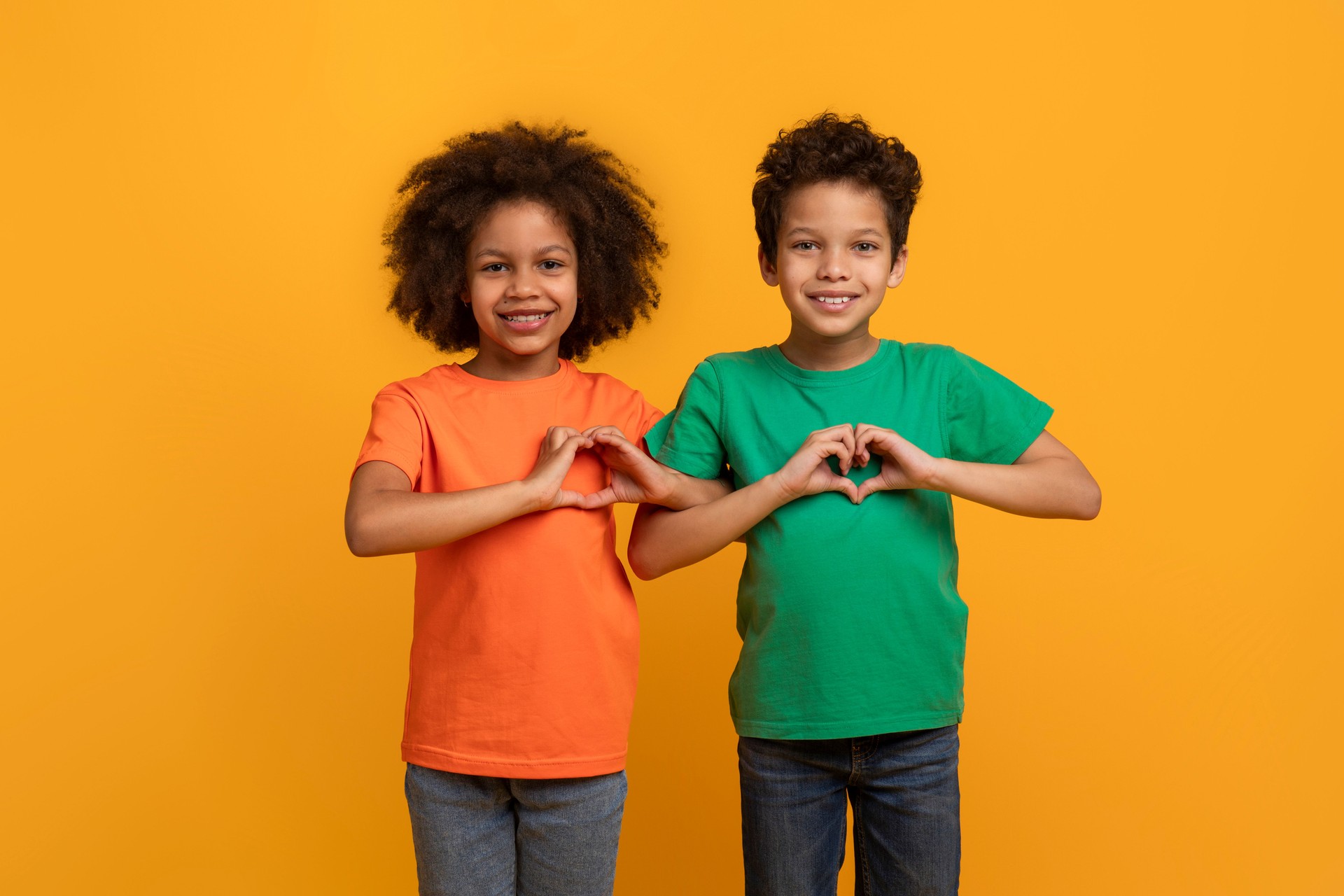 Two Children Making Heart Shape in Front of Yellow Wall